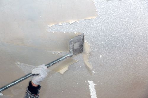 man scraping off popcorn-textured ceiling